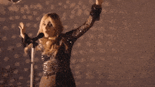 a woman singing into a microphone while holding her hair