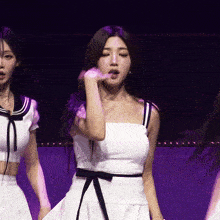 a woman in a white dress with a black ribbon around her waist is dancing on a stage
