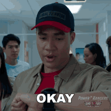 a man wearing a power rangers hat is holding a watch and saying okay