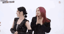 two girls with pink hair are standing next to each other and clapping their hands .