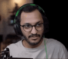 a man with glasses and headphones is sitting in front of a computer screen .