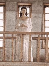 a woman in a white dress is standing on a wooden railing