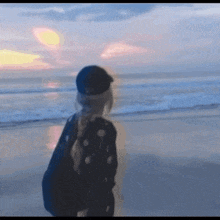 a girl in a black hat stands on a beach