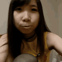 a woman wearing a yellow tank top with a bird on it looks at the camera