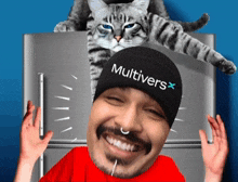 a man wearing a beanie that says multivers stands in front of a cat on top of a refrigerator