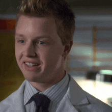 a man wearing a white lab coat and tie smiles