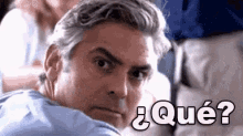 a man is sitting on a plane and looking over his shoulder at the camera with the words ¿ qué ? on the bottom .