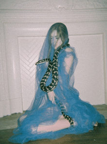 a woman in a blue dress is holding a snake around her neck