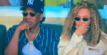 a man and a woman are sitting next to each other and the man is wearing a ny hat .