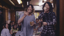 a man in a plaid shirt holds a glass of beer while standing next to another man