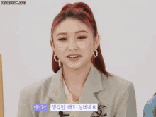 a woman with red hair is wearing a jacket and earrings .