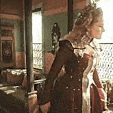 a woman in a red dress with a crown on her head stands in front of a window