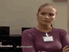 a woman in a purple sweater with a name tag on her neck is looking at the camera .