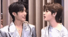 two young men are standing next to each other and talking to each other in a room .