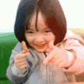 a little girl is smiling and pointing at the camera while holding a piece of food .