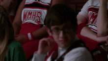 a man wearing glasses sits in a crowd wearing a vmhs shirt