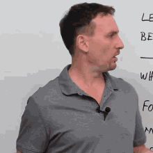 a man in a grey shirt stands in front of a whiteboard that says " le be " on it