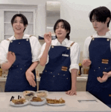 three men wearing blue aprons are standing around a table with plates of food