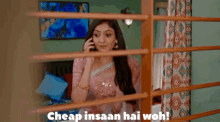 a woman in a saree is talking on a cell phone behind a fence with the caption cheap insaan hai woh