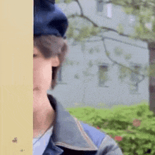 a man wearing a blue hat and a denim jacket is standing next to a wall .