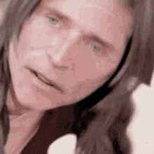 a close up of a man 's face with long hair and green eyes looking at the camera .