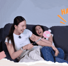 two women are sitting on a couch with one wearing a shirt that says ' sd ' on it