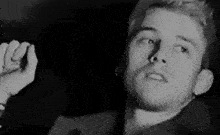 a black and white photo of a man with a beard holding his hand up in the air .