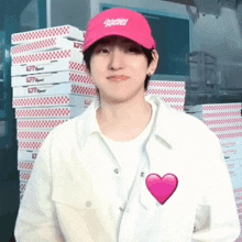 a man wearing a pink hat and a white jacket is standing in front of stacks of pizza boxes .