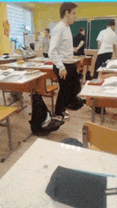 a boy in a white shirt is standing in a classroom surrounded by desks .