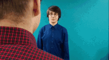 a man in a blue shirt looks at another man in a plaid shirt