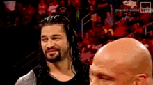 a man with a beard and a bald head is standing next to another man in a crowd .