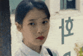 a woman in a white shirt stands in front of a window with chinese writing