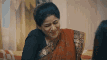 a woman in a red saree is sitting on a bed with a woman .