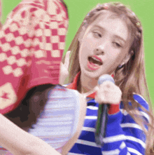 a girl singing into a microphone with a checkered hat behind her