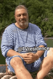 a man wearing a striped shirt and shorts is sitting on a rock with the words @tvresidence above him .