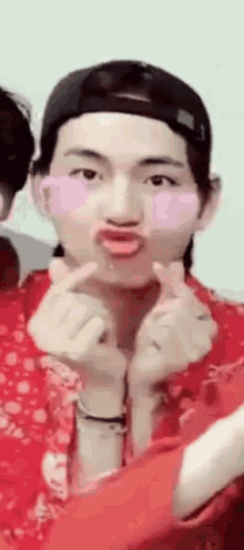 a man wearing a baseball cap and a red shirt is making a heart with his hands .