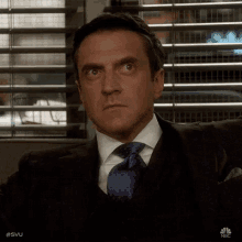 a man in a suit and tie is sitting in front of a window looking up .