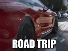a red car is driving down a street with the words road trip written on the side of it
