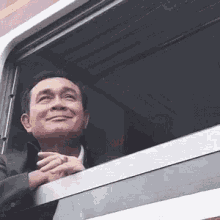 a man in a suit is looking out of a train window and smiling .