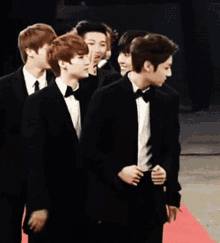 a group of young men wearing tuxedos and bow ties are walking on a red carpet
