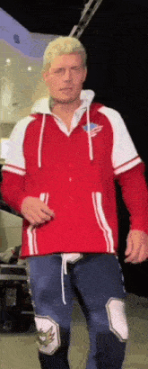 a man wearing a red and white hoodie and blue pants is walking in a room .
