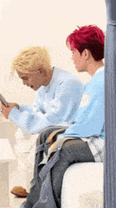 two men are sitting next to each other on a couch and one of them is looking at his phone .