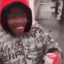 a man wearing a red hat and a hoodie is smiling while holding a bottle of soda .