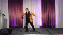a man in a yellow jacket is dancing on a stage with purple curtains behind him