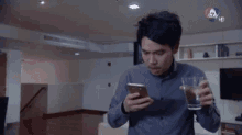 a man is drinking a glass of water while looking at his phone .
