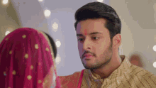 a man with a red dot on his forehead is looking at a woman in a pink veil .