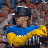 a baseball player wearing a helmet and yellow gloves is standing in front of a crowd .