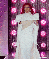 a drag queen wearing a white dress and white gloves is standing on a stage .