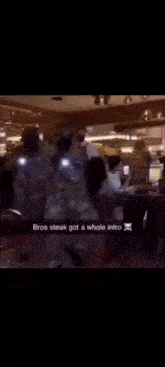 a man in a white shirt is standing in front of a group of people and says " bros steak got a whole intro " .