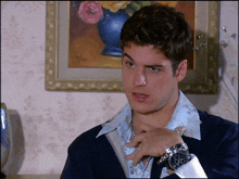 a man wearing a watch adjusts his tie in front of a framed painting